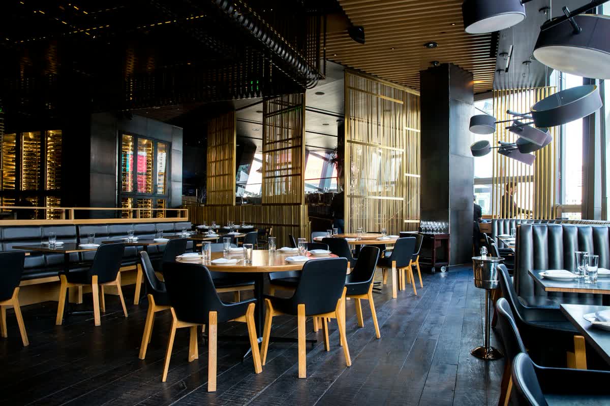 Comedor de restaurante con mesas vacías, sillas y luz cálida sobre el suelo de madera